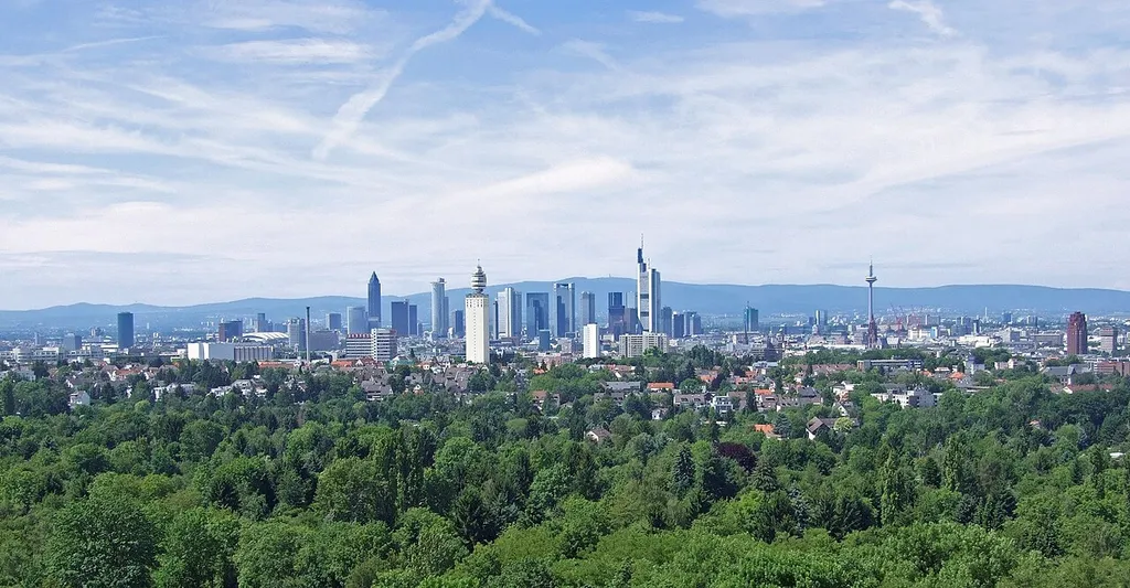 The skyline of Frankfurt-am-Main, Germany, viewed from south, from the tower Goetheturm (destroyed in 2017). In the foreground a part of the city’s municipal forest, Frankfurter Stadtwald. In the background some of the regional hills of Hesse, the Taunus. The large houses on either side of the photo – the Westhafen Tower on the left and the Main Plaza Tower on the far right (please refer to the accompanying image notes) – mark the path of the river Main through the city from east to west.