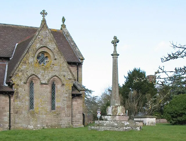 Part of St Peter's parish church, Lugwardine, Herefordshire. On the left is the south chapel attached to the chancel. On the right is the churchyard cross, which has an early 20th-century shaft and head on a 14th- or 15th-century base and steps.