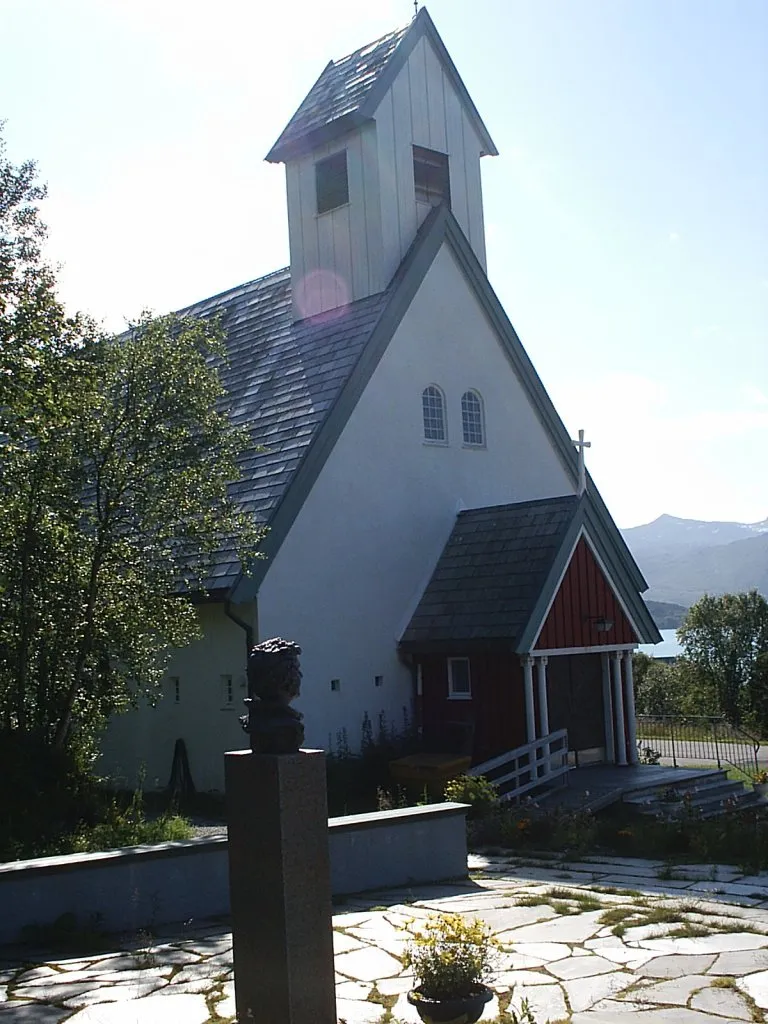 Berg kirke på Senja. I forgrunnen står en minnestøtte for Ingrid Bjerkås