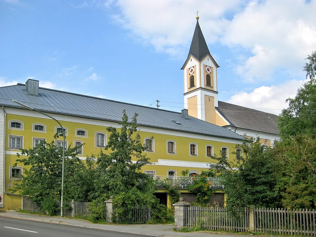 Breitenberg, historic grocery store with Parish Church of St Raymond of Peñafort in background.