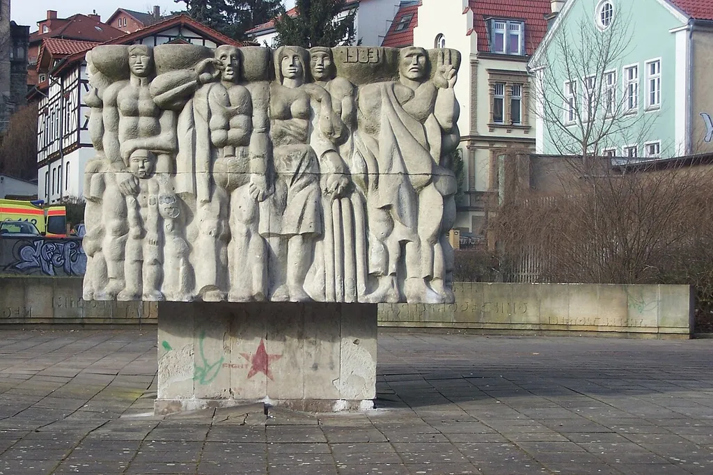 Das Bildmotiv (1983) symbolisiert das Karl-Marx-Jahr 1983 - zugleich das Jahr der Denkmalseinweihung. Neben dem vierflächigen Betonkubus erkennt man im Hintergrund einen Abschnitt der mit Brecht-Zitaten ausgestalteten Platzumrandung.