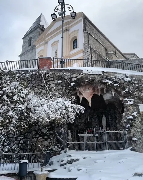 the façade with the statue of Virgin Mary dominates a square that serves as a roof to the cave below.