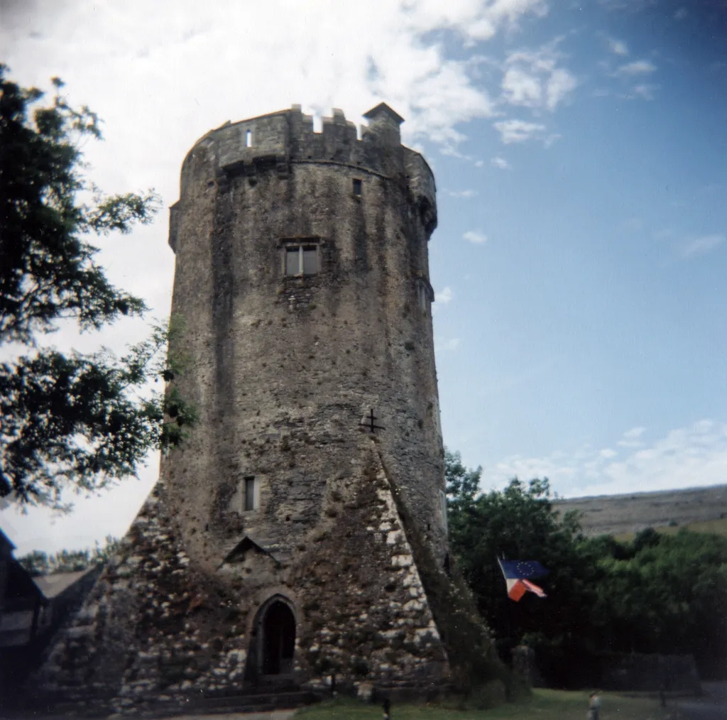 Like a rocket on its launch-pad, this unusual sixteenth century tower house takes the form of a cylinder impaled upon a pyramid. The whole base of the wall between the four boldly projecting spurs is commanded by shotholes ingeniously placed in the apex of pointed notches at the fusion of the cylinder and pyramid. One of these notches, or ghost-gables, lies over the door which is also commanded by one of four machicolations projecting from the parapet. Internally, the tower has five storeys with dome vaults over the ground and third stories, both of which have well-preserved impressions of wickerwork matting. The hall on the fourth story has mullioned windows with the spiral stair projecting into the room. The top floor, originally a bed chamber, has now been incorrectly restored as a gallery, presumably so that visitors can admire the new conical oak roof.