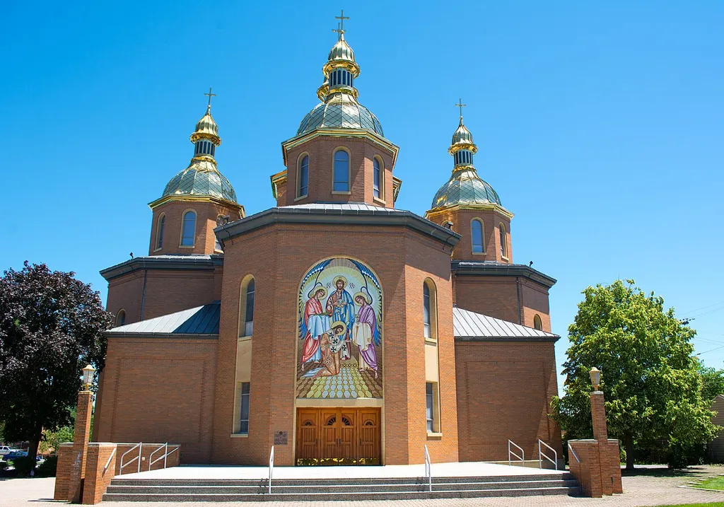 The main entrance to St. Josaphat Ukrainian Catholic Cathedral in Parma, Ohio, in the United States. Sts. Peter and Paul Ukrainian Catholic Church of Cleveland purchased 10.5 acres of land at 5720 State Road in Parma in 1947. The church broke ground in March 1949 for a new Catholic school, which opened in May 1951. The school's chapel served as a mission church. A second school building (the “Annex") and a convent for the Sisters of St. Basil the Great opened in May 1954. On August 13, 1959, Archbishop Constantine Bohachevsky erected St. Josaphat Parish. Rev. Andrew Ulicky was named the first pastor, and the school name changed to St. Josaphat. In 1961, St. Josaphat Parish began construction of a building intended to house a co-educational high school. The $1 million structure was built completely through volunteer labor, and was designed by parish member Michael Stefanyk (an architect and engineer). Made of brick with stone trim, the building featured an open beam wooden ceiling. It was circular, 211 feet in diameter. Sixteen classrooms, a library, and a science laboratory occupied the outer ring of the building, while a 140 foot diameter gymnasium occupied the center. The dome had a height of 48 feet at its highest point, 25 feet at its lowest. The dome was designed by Roof Structures, Inc. of St. Louis. The 4 x 10 precut wooden beams were shipped from Oregon. The basement originally was designed to be a nuclear fallout shelter. Construction on the school was still under way in 1964. By that time, half the fallout shelter had been taken over by HVAC equipment and the other half converted into an art room and a cafeteria. Completed by 1968, the school never opened. The erection of St. Andrew Parish siphoned off too many familes. Instead, the structure served as a sports venue (primarily boxing), auditorium, and meeting hall. About 1975, it became known as the "Astrodome". A third, five-classroom school building was erected in 1965. St. Josaphat Chapel suffered a ma