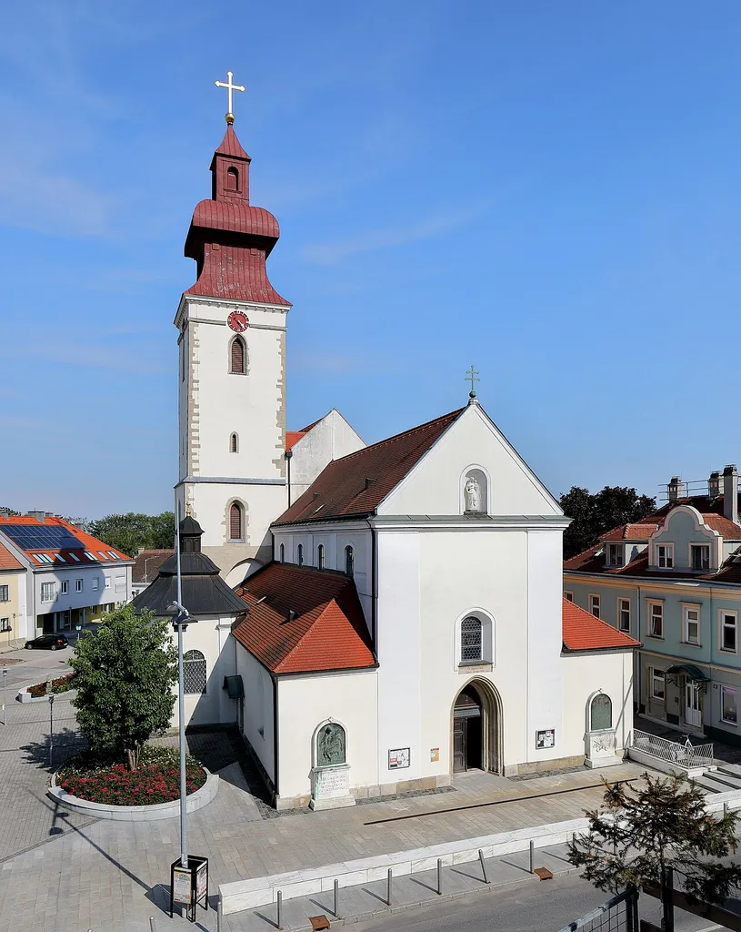 Nordwestansicht der röm.-kath. Pfarrkirche Maria Schutz in der niederösterreichischen Stadtgemeinde Groß-Enzersdorf. Eine ehemalige Wehrkirche mit wuchtigem Nordturm, die in der 2. Hälfte des 17. Jahrhunderts brockisiert wurde. Das Langhaus wurde Ende des 13. Jahrhunderts errichtet und der erhöhte Chor Ende des 14. Jahrhunderts. Die Sakristei und der Kapellenanbau wurden in der Barockzeit errichtet.