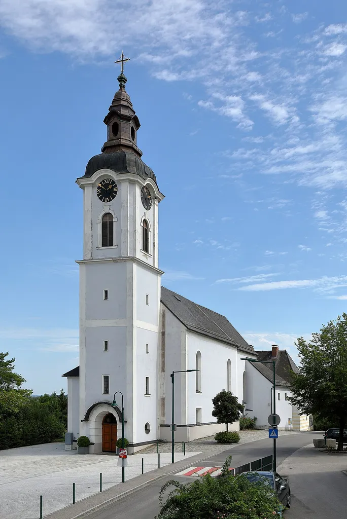 Westansicht der röm.-kath. Pfarrkirche hl. Wolfgang in Öhling, ein Ortsteil der niederösterreichischen Marktgemeinde Oed-Oehling.Eine schlichte im Kern barocke Saalkirche in erhöhter Lage. Nach einem Brand im Jahr 1816 war sie eine Brandruine und wurde 1833 wiedererrichtet. Der wuchtige neobarocke vorgestellte Westturm stammt aus dem Jahr 1914.