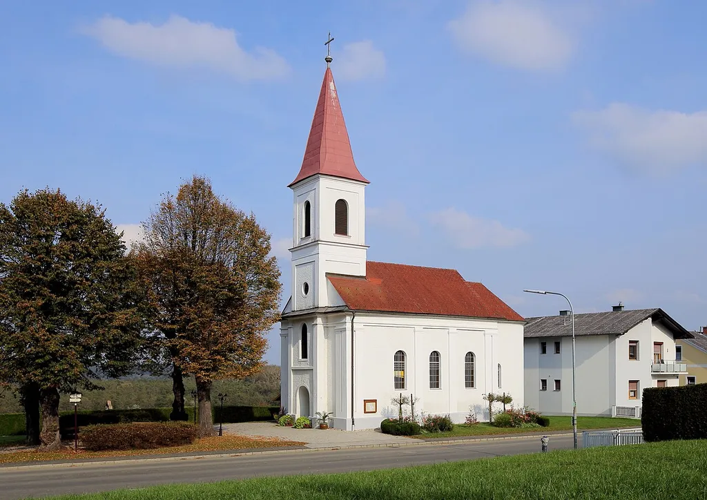 Südwestansicht der Filialkirche St. Nikolaus in der burgenländischen Bezirkshauptstadt Güssing (Ortsteil St. Nikolaus). Nachdem die Vorgängerkirche bei einem Brand 1897 vollständig abgebrannt ist, wurde die Kirche neu errichtet und am 22. September 1907 vom Erzpriester Kanonikus Franz Baumgartner eingeweiht. Die 4 Linden vor der Kirche wurden 1908 gepflanzt.