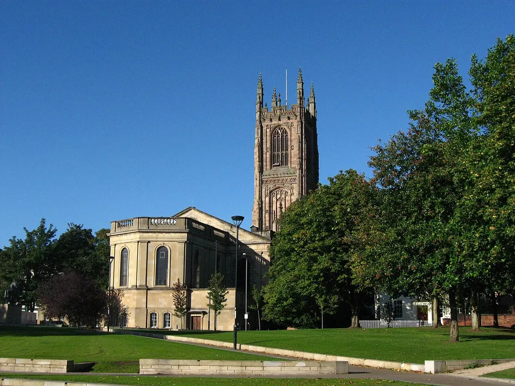 View of Derby Cathedral, England, looking west from Cathedral Green. The 65m high tower dates from the 1530s, the nave from 1725 and the retrochoir from the 1970s. The latter is made from artificial sandstone, whereas the nave and tower are of Derbyshire Millstone Grit. A peregrine falcon nest platform is just visible in lower left corner of bell tower louvres. Cathedral Green was redeveloped and opened as a new public open space in 2009. A statue of Bonnie Prince Cahrlie on horseback is visible in the extreme left of the image
