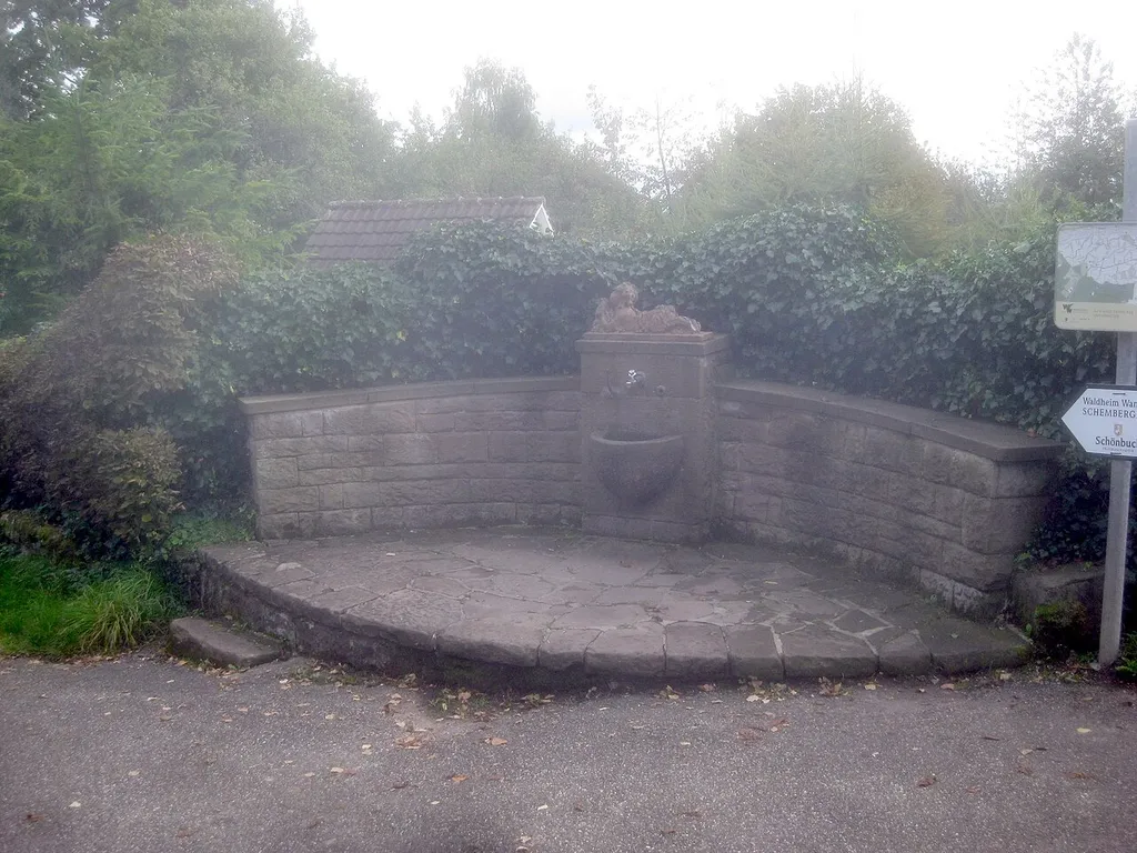 Burgbrünnele mit Brunnenfigur von de:Josef Zeitler, am Ende des Rennweges in Stuttgart-Wangen an der Stelle der ehemaligen de:Burg Hedelfingen. Konkav geschwungene Mauer mit quaderförmigem Brunnenstock und halbkugelförmigem Brunnentrog, Bekrönung des Brunnenstocks ist eine liegende Flötenspielerputte mit Bocksbeinen. Standort: siehe File:Stuttgart-Wangen, 0001.jpg.