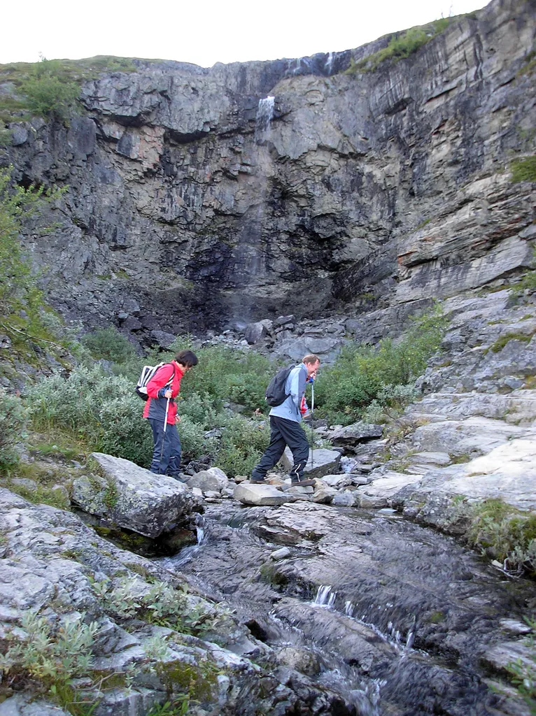 Two hikers and Kitsiputous waterfall, one of the main attractions of Malla Nature Reserve in Enontekiö, Finland. Due to the picture having been taken in late summer, there's only little water flowing.