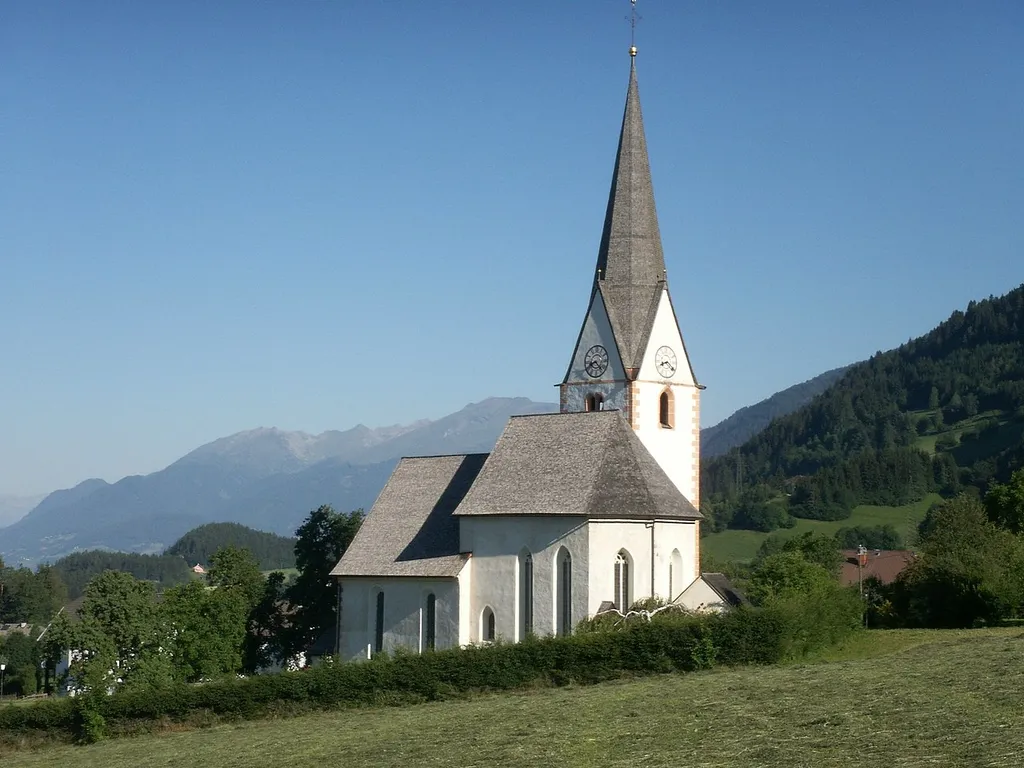 Church in Matzelsdorf in Carinthia / Austria / European Union. Matzelsdorf is a village in the community of Millstatt. In the background the first mountains of the Hohe Tauern. Search items: haymaking, shingle roofs, gothic church tower with clock.